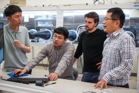 Xiaodong Xu in a lab talking to three students.